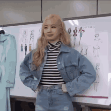 a woman in a striped shirt and denim jacket is standing in front of a whiteboard .