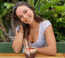 a woman sits at a table with a cup of food and a spoon in it