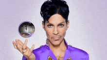 a man in a purple shirt is holding a silver ball with a purple letter p on it