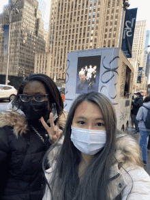 two women wearing face masks pose for a picture in front of a sign that says ' sr ' on it