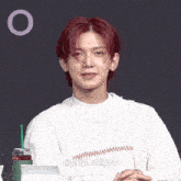 a man with red hair is wearing a white sweater and a green cup