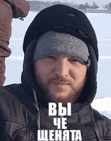 a man with a beard wearing a hooded jacket and a beanie with the words " вы " on the bottom