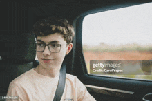 a young man wearing glasses is sitting in the back seat of a car looking out the window .