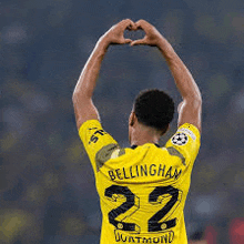 a man wearing a yellow shirt with the number 22 on it making a heart shape with his hands