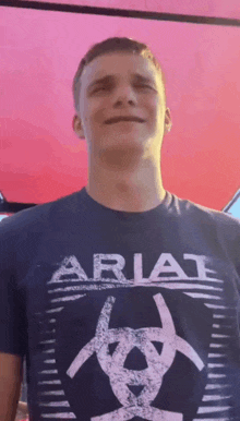 a man wearing a blue ariat t-shirt stands in front of a red background