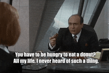 a man in a suit and tie talks to a woman while holding a donut in his hand