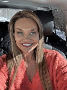 a woman in a red sweater is smiling while sitting in a car