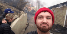 a man wearing a red hat is taking a selfie in front of a burning building