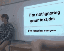 a man sits in front of a projector screen that says " i 'm not ignoring your text/dm "