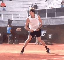 a man in a white tank top and black shorts is holding a tennis racquet on a tennis court sponsored by atp