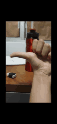 a person 's hand is pointing to a red bottle on a desk