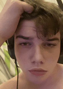 a young man wearing headphones holds his hand to his forehead