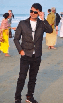 a man wearing sunglasses and a black jacket is standing on a beach