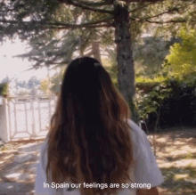 a woman in a white shirt is standing in front of trees with the words in spain our feelings are so strong