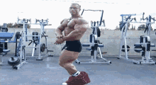 a muscular man stands in front of a row of gym equipment including a machine that has the letter a on it