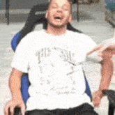 a man in a white shirt is sitting in a chair with his mouth open .