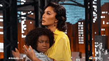 a woman in a yellow dress is holding a little boy in her arms .