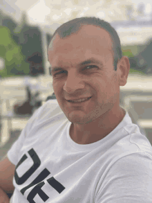 a man wearing a white t-shirt with the letter ue on it smiles for the camera