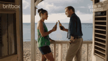 a man and a woman toasting on a balcony with the words death in paradise series eight on the bottom