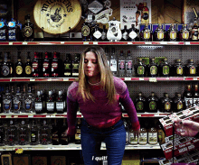 a woman is standing in front of a shelf full of liquor bottles and a sign that says bottled in america on it