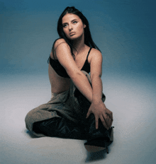 a woman in a black bra and pants sits on the floor