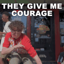 a man in a red shirt is kneeling down in front of a sign that says " they give me courage "