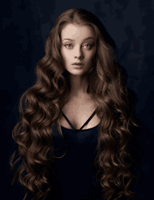 a woman with long curly hair is wearing a black dress