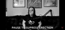 a black and white photo of a man sitting on a couch with the words pause to suppress erection above him