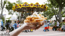 a person holding a bowl of french fries in front of a carousel with the word delish on the bottom right