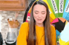 a woman in a yellow sweater is standing in a kitchen with her eyes closed and a blender in the background .