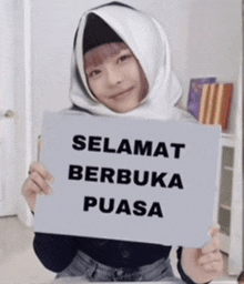 a girl wearing a hijab holds up a sign that says selamat berbuka puasa