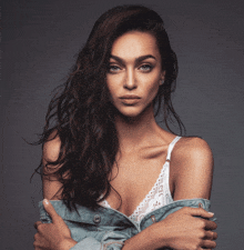 a woman wearing a white bra and a denim jacket looks at the camera