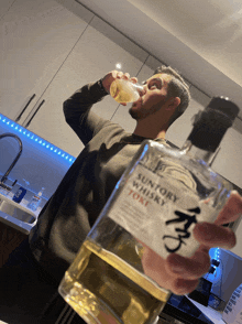 a man drinking from a bottle of suntory whisky