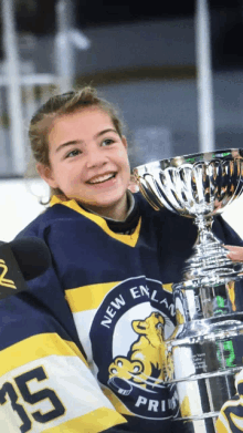 a young girl in a new england jersey holds a trophy