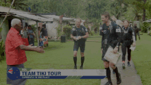 a man shakes hands with another man in front of a banner that says nzl team tiki tour currently in 3rd place