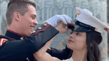 a man in a marine uniform is putting a hat on a woman 's head .