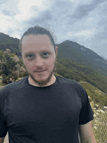 a man with a beard wearing a black shirt is standing in front of a mountain