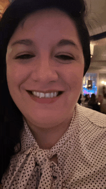 a woman wearing a white and black polka dot shirt smiles for the camera