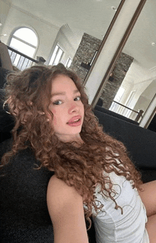 a woman with curly hair is sitting on a couch in front of a mirror