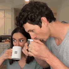 a man kisses a woman on the nose while drinking from a white mug with the letter b on it