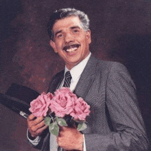 a man in a suit and tie is smiling while holding a bouquet of pink roses .