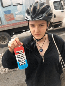 a young woman wearing a helmet is holding a bottle of prime energy drink .