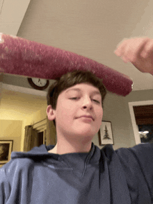 a boy in a blue shirt is holding a rolled up sausage on top of his head