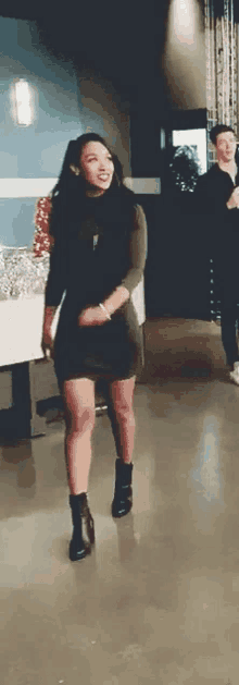 a woman in a black dress and black boots is standing on a concrete floor in a room .