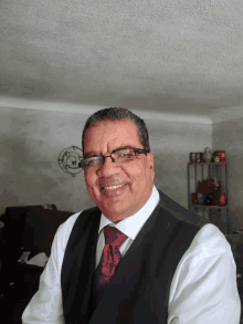 a man wearing glasses and a black vest smiles for the camera