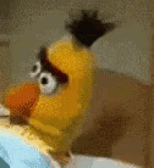 a yellow angry bird with big eyes and a crown on its head is sitting on a bed .