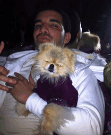 a man is holding a small dog that is wearing a purple dress