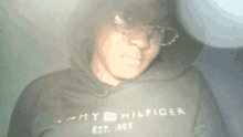 a man wearing a black tommy hilfiger hoodie and glasses