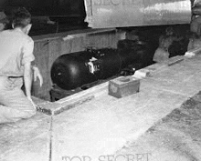 a man is kneeling down next to a large bomb on the ground .