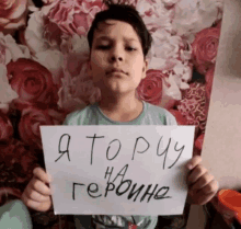 a young boy holds up a sign in front of a wall of roses